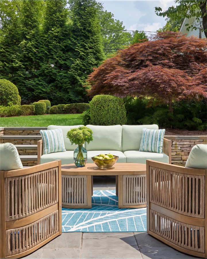 Outdoor lifestyle photography of a teak patio furniture set staged in a landscaped backyard